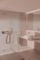 Badezimmeransicht mit Dusche und Waschbecken. Die Dusche ist mit einer runden Regenbrause von Ideal Standard ausgestattet. Weiße Armaturen und sanfte Lichtakzente ergänzen den Raum.